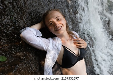 The Sun's Rays On Her Face Are A Smiling Red-haired Woman Looking At The Camera Near The Waterfall.