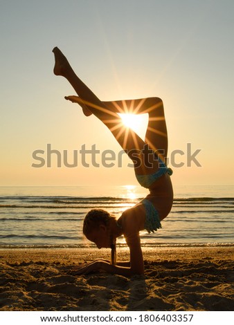 The sun's rays shine through the legs of a gymnast on the beach. The girl performs a handstand and holds her legs in the shape of a triangle. Sunset at sea.