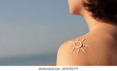 sunscreen banner, summer skin care, the girl is sitting on the beach against the background of the sea, she has a sun painted with cream on her shoulder - Powered by Shutterstock