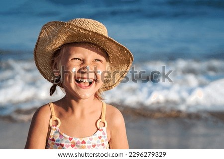 Sunscreen for Children. Tanned Girl Child with Cream on Face Smiling Having fun Sunbathing on Sea Beach Background. Sun Protection Sunblock Skin Care concept.