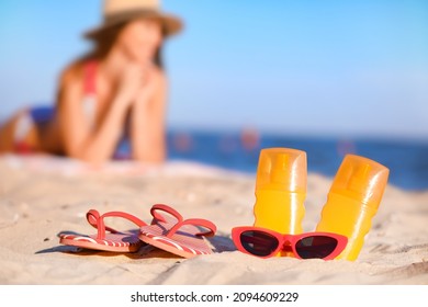Sunscreen cream, sunglasses and flip-flops on beach sand