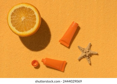 Sunscreen, half an orange and a starfish on a sandy background. A preparation to protect the skin from sunlight. - Powered by Shutterstock