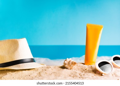 Sunscreen lotion on sandy beach, summer composition with hat, sunglasses and shells, blue sea as background, copy space. Summer vacation and skin care concept, spf uv-protect cosmetic.