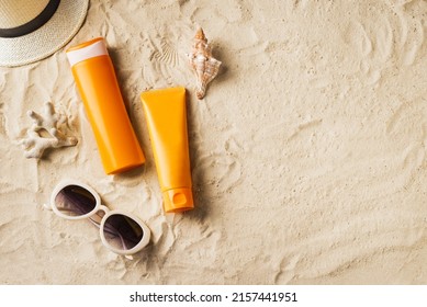 Sunscreen lotion, sunblock cream, sunglasses and hat on sandy beach as background, top view, copy space. Summer vacation and skin care concept, spf uv-protect cosmetic products.