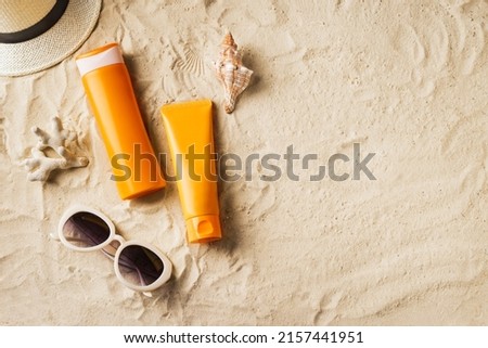 Sunscreen lotion, sunblock cream, sunglasses and hat on sandy beach as background, top view, copy space. Summer vacation and skin care concept, spf uv-protect cosmetic products.