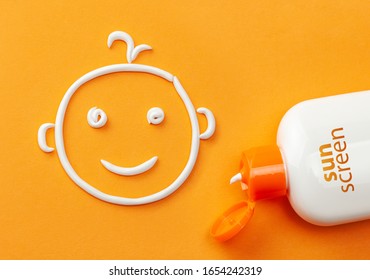 Sunscreen On Orange Background. Plastic Bottle Of Sun Protection And White Cream In The Shape Of A Smiling Baby Face. Cream For Kids