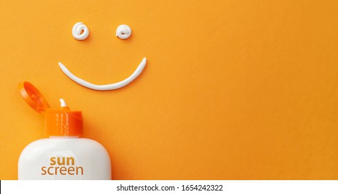 Sunscreen on orange background. Plastic bottle of sun protection and white cream in the shape of Smiley, smiling face.