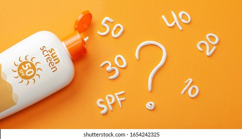Sunscreen on orange background. Plastic bottle of sun protection and white cream in the form of question mark and numbers SPF. How to choose a sunscreen.