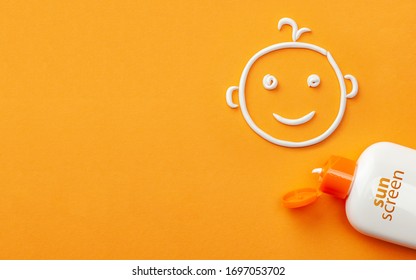 Sunscreen On Orange Background. Plastic Bottle Of Sun Protection And White Cream In The Shape Of A Smiling Baby Face. Cream For Kids