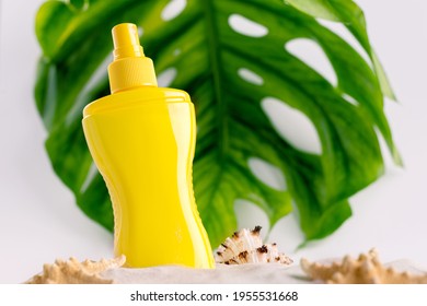 Sunscreen Spray Bottle On A Sandy Beach Decorated With Different Seashells Against Big Monstera Leaf Background.