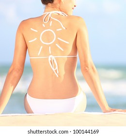 Sunscreen / sun tan lotion sun drawing woman back  Girl in bikini sitting beach in sunlight 