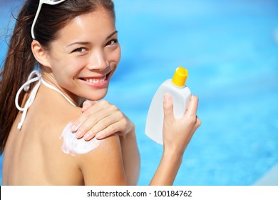 Sunscreen / sunblock. Woman putting solar cream on shoulder smiling happy outdoors by pool under sunshine on beautiful summer day. Mixed race Asian / Caucasian girl. - Powered by Shutterstock