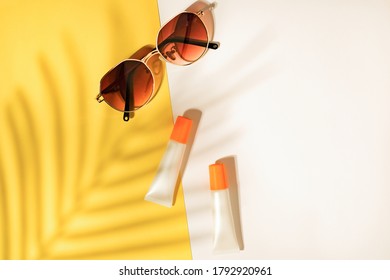 Sunscreen tube with sunglasses on tropical leaf shadow background . Skincare for summer and travel.