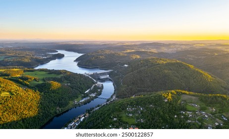 A sunset aerial shot of Orlik Reservoir in Czechia shows a winding river, hills, and a quaint town in the valley with vibrant blue and golden skies. - Powered by Shutterstock