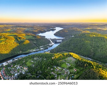 A sunset aerial shot of Orlik Reservoir in Czechia shows a winding river, hills, and a quaint town in the valley with vibrant blue and golden skies. - Powered by Shutterstock