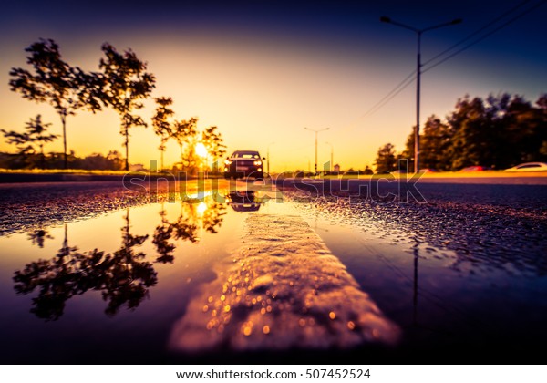 Sunset after rain, the car on the highway. Wide\
angle view of the dividing line level in a puddle, image vignetting\
and the orange-purple\
toning