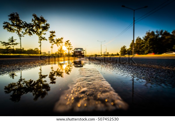 Sunset after\
rain, the car on the highway. Wide angle view of the dividing line\
level in a puddle, image\
vignetting