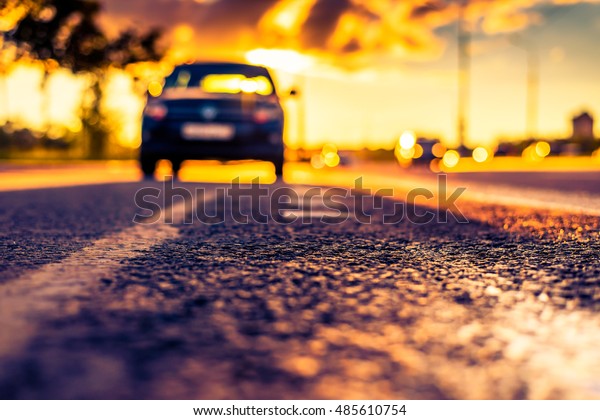 Sunset after rain, the car parked on the roadside.\
Close up view from the level of the dividing line, image in the\
orange-purple toning