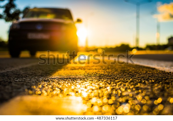 Sunset after rain, the\
car parked on the roadside. Close up view from the level of the\
dividing line, bokeh 