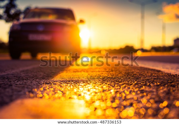 Sunset after rain, the car parked on the roadside.\
Close up view from the level of the dividing line, image in the\
orange-purple toning