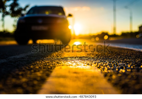 Sunset after rain, the car\
parked on the roadside. Close up view from the level of the\
dividing line