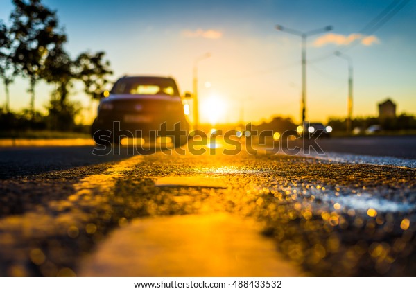 Sunset after rain, the car parked on the\
roadside and headlights of the driving cars on the highway. Close\
up view from the level of the dividing\
line
