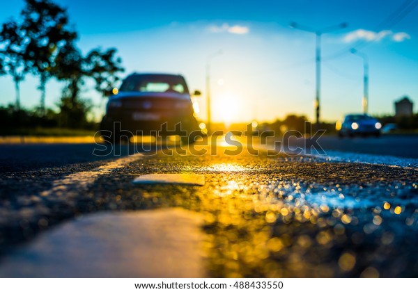 Sunset after rain, the car parked on the\
roadside and headlights of the driving car on the highway. Close up\
view from the level of the dividing\
line
