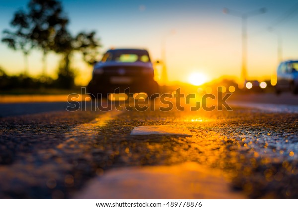 Sunset after rain, the car parked on the\
roadside and headlights of the driving cars on the highway. Close\
up view from the level of the dividing\
line