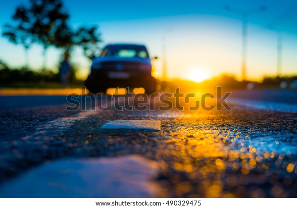Sunset after rain, the car\
parked on the roadside. Close up view from the level of the\
dividing line
