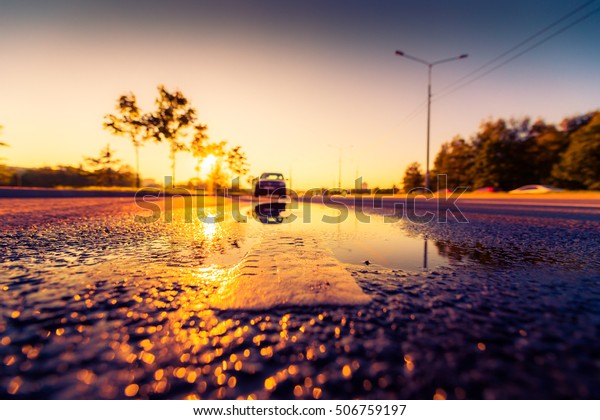 Sunset after rain, the car parked on the roadside.\
Wide angle view of the level of the dividing line, image in the\
orange-purple toning