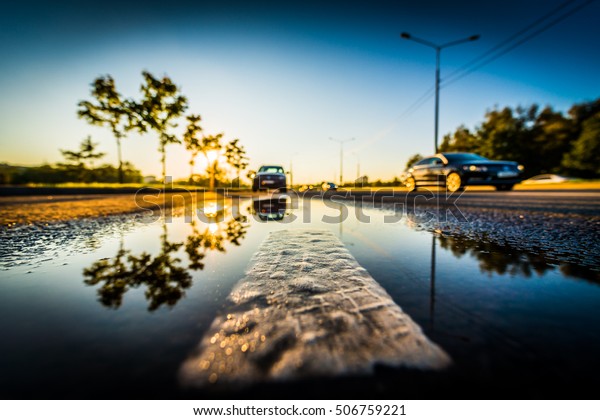 Sunset after rain, the car parked on the roadside\
and driving cars on the highway. Wide angle view of the dividing\
line level in a puddle