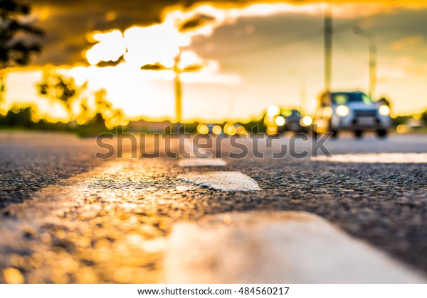Sunset after rain, the cars\
driving on the highway. Close up view from the level of the\
dividing line