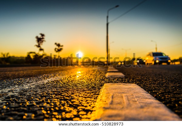 Sunset after\
rain, the cars driving on the highway. Wide angle view of a\
close-up from the level of the dividing\
line