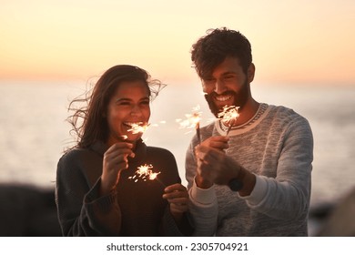 Sunset, beach and couple with fireworks for celebration, party and sparks on romantic date. Nature, love and happy man and woman with sparklers for honeymoon on holiday, weekend and vacation - Powered by Shutterstock