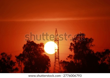 Sunset behind communication tower with trees silhouetted in vibrant orange sky