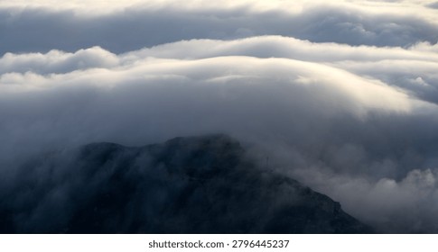 Sunset behind layered clouds over mountains. Golden light breaks through sky, creating a peaceful and dramatic silhouette scene.