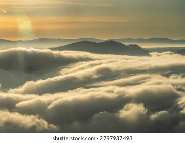 Sunset behind layered clouds over mountains. Golden light breaks through sky, creating a peaceful and dramatic silhouette scene.