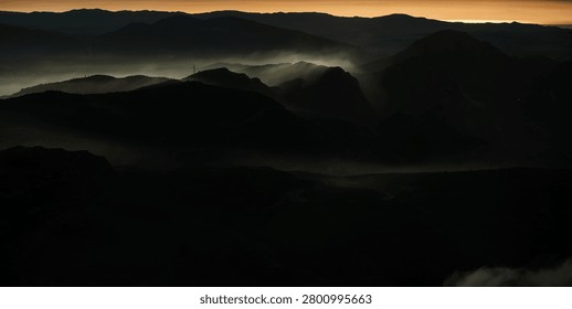 Sunset behind layered clouds over mountains. Golden light breaks through sky, creating a peaceful and dramatic silhouette scene.