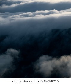 Sunset behind layered clouds over mountains. Golden light breaks through sky, creating a peaceful and dramatic silhouette scene.
