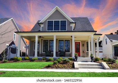 Sunset behind a Single-Family Suburban Craftsman House with Big Front Porch, White Pillars, and a Red Front Door.