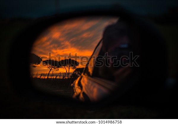 A\
sunset behind the trees through the mirror of the\
car