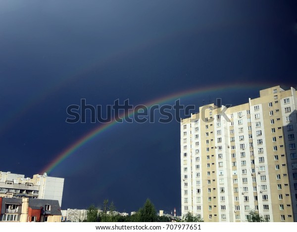 Sunset and\
black rain clouds in sky above homes and buildings before raining\
in city, raining season,city scape, sunset background Rain street. \
Rainbow over the city on Rainy day.\
