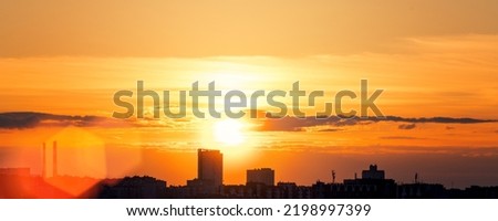 Sunset with bright sun rays over urban buildings silhouettes. Cityscape in evening time.