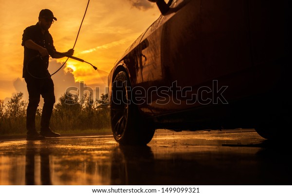 Sunset Car\
Washing. Caucasian Men in His 30s Cleaning His Modern Car Using\
Pressure Washer. Automotive Industry\
Theme.
