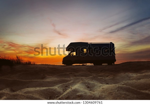 Sunset and caravan silhouette.\
Van life concept. Travelling in the Europe. Camper van on the\
beach.