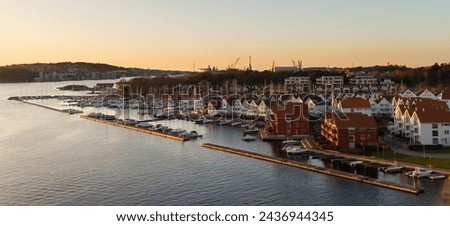 Sunset casts a golden glow on a coastal town, illuminating docked boats and traditional houses.