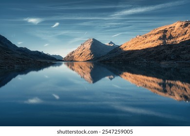 Sunset casts a serene glow on mountain peaks mirrored in a tranquil alpine lake in autumn. Lake Bianco, Switzerland in fall. Landscape with mountains, reflection in water, blue sky. Picturesque scene - Powered by Shutterstock