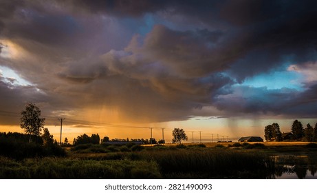 Sunset casts warm light over a serene lake, with dark clouds and sunlight rays visible, framed by trees and distant power lines in the background