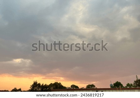 Sunset in the city with cloudy sky, gray clouds and the reflection of the sun on the horizon, over a building surrounded by tall, leafy trees