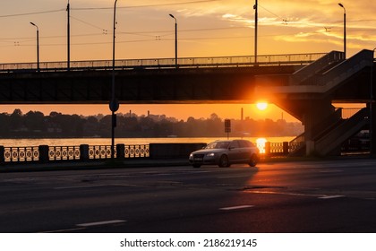 Sunset In City. Golden Light Over The Bridge On Street With Driving Car. Riga, Latvia, 06.08.2022